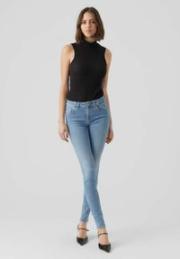 Fekete bordázott ujjatlan blúz világoskék skinny farmerral párosítva. A modellen fekete hegyes sarkú cipő van. Simás textúrák, testhezálló dizájn, laza stílus.