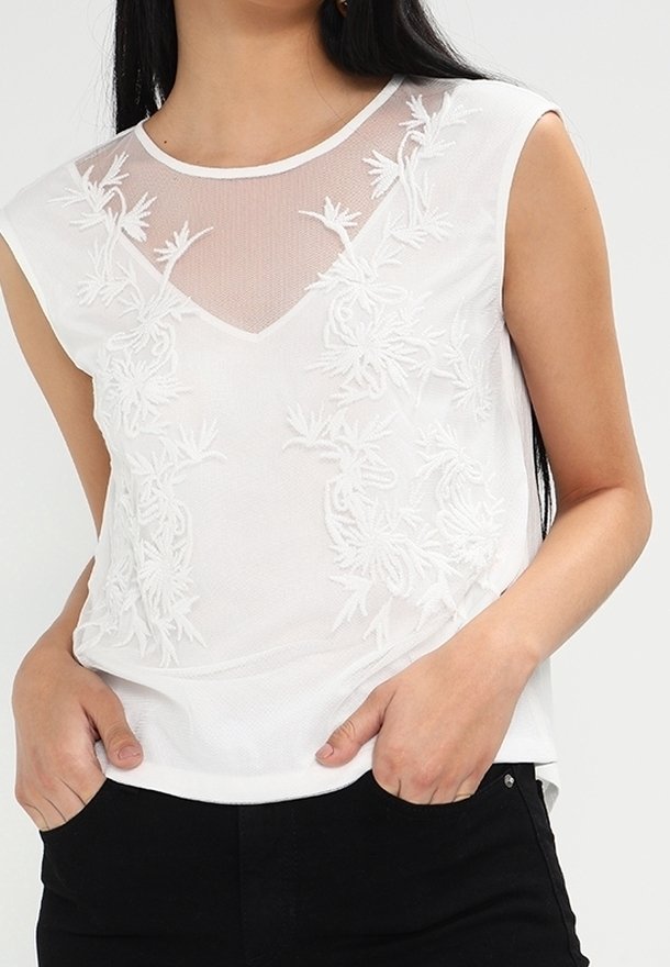 Biała bluzka bez rękawów z przezroczystym siateczkowym dekoltem i kwiatowymi haftami. Miękki materiał o luźnym kroju i kształcie w literę V.