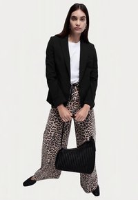 Blazer nero aderente sopra una t-shirt bianca, abbinato a pantaloni larghi con stampa leopardata. Tiene una borsa nera intrecciata, indossa scarpe nere.