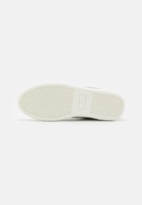 Sole of a sneaker, featuring a white rubber material with a herringbone tread pattern, smooth finish, and a brand logo in the center.