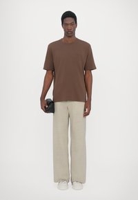 Brown short-sleeve t-shirt paired with light beige wide-leg trousers, held with a black textured clutch, featuring a relaxed fit.