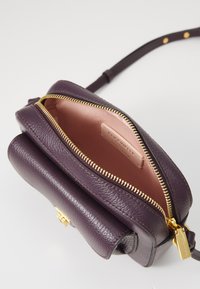 Purple leather handbag with a textured surface, gold zipper, and smooth interior lining. Features a short strap and embossed logo inside.