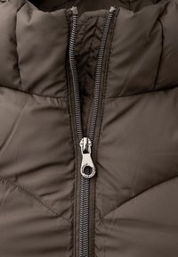 Chaqueta acolchada marrón con cuello alto, cremallera plateada y textura acolchada. La cremallera baja verticalmente por el centro.