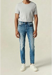 Camiseta de cuello redondo color gris claro combinada con jeans ajustados descoloridos de tono azul medio. El modelo lleva zapatillas blancas. Diseño casual y moderno.