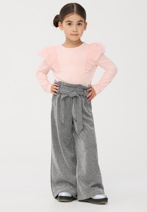 Maglietta lunga a maniche corte di colore rosa chiaro con dettagli arricciati e pantaloni grigi a gamba larga con cintura legata, abbinati a scarpe lucide nere e argentate.