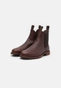 Botas Chelsea de cuero marrón con paneles laterales elásticos, lengüetas para facilitar el calzado y una suela texturizada resistente. Acento en el tacón de madera.
