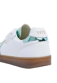 Valge tennisekenk teal'roheliste aktsentidega, sile sünteetiline materjal, ümmargune varvas, lame pruun kummist talla, ning tõstetud "1973" detail kannal.
