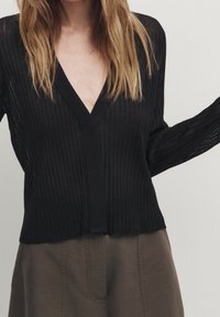 Schwarze gerippte Strickjacke mit V-Ausschnitt, langen Ärmeln und Knopfverschluss, die eine transparente Textur und eine lockere Passform aufweist.