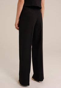 Črne široke hlače z gladko teksturo, s poudarjenim pasom in zadnjima žepoma. Rob hlač je nad čevlji.