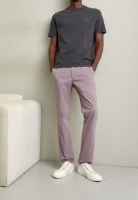 Szara bawełniana koszulka z prążkowanym, okrągłym dekoltem, zestawiona z jasnofioletowymi bawełnianymi spodniami i białymi trampkami z wielokolorowymi oczkami.