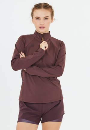 Haut de sport marron à manches longues avec un col zippé quart et des manches raglan, associé à un short marron assorti avec une subtile accentuation.