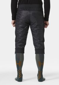 Czarne spodenki z ociepleniem i teksturowanym wzorem, elastyczny pasek w talii oraz kieszeń na zamek. W połączeniu z zielono-brązowymi skarpetkami do kolan w wzór.