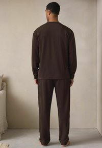 Brązowa koszula z długim rękawem z okrągłym dekoltem oraz pasujące luźne spodnie. Gładka tekstura, prosty design i luźna sylwetka.