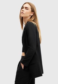 Blazer nero con una vestibilità su misura, caratterizzato da maniche lunghe, una tasca singola e un design corto. Texture liscia e stile minimalista.
