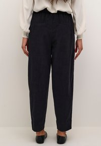 Donker marineblauwe broek met wijde pijpen van een gestructureerde stof. Rekbare tailleband en twee achterzakken, afgewerkte randen, gecombineerd met eenvoudige zwarte flats.