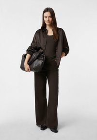 Braunes Satin-Knopfhemd, dunkles Tanktop und weit geschnittene Hose, kombiniert mit einer großen schwarzen Handtasche mit gewebter Textur.