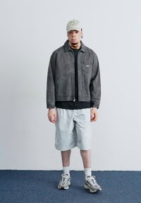 Gray zip-up jacket over a black shirt, white shorts, and light sneakers. Accessories include a beige cap. Smooth texture, modern design.