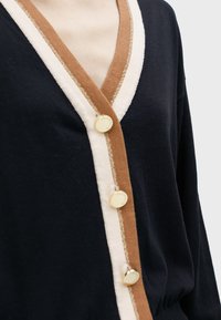 Black cardigan featuring a V-neck, brown and cream accents, gold buttons, and a soft texture with a slight sheen.