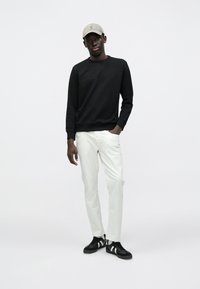 Μαύρο φούτερ, ανοιχτό γκρι καπέλο, λευκό παντελόνι και μαύρα αθλητικά παπούτσια με λευκές ρίγες. Απλό σχέδιο, ορατή υφή υφάσματος.