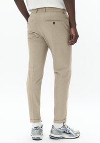 Pantaloni personalizați bej, cu o textură netedă, având buzunare la spate și o croială slim, asortați cu adidași gri și albastri.