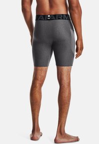 Shorts de sport gris à coupe près du corps, fabriqués en tissu lisse et extensible. Présente une taille élastique noire avec logo et une poche latérale.
