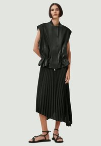 Melnās peplum vestes ar vertikālajām krokām un rāvējslēdzēja aizdari, apvienotas ar melnu plīvētu svārku ar asimetrisku apakšmalu, valkātas ar sandaļiem ar lencēm.