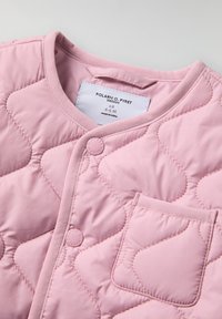 Vaaleanpunainen tikkitakki, jossa on pyöreä kaula-aukko, nepparikiinnitys ja pieni rintatasku. Pehmeä rakenne ja vino ompelukaavio. Brändilappu näkyvissä.