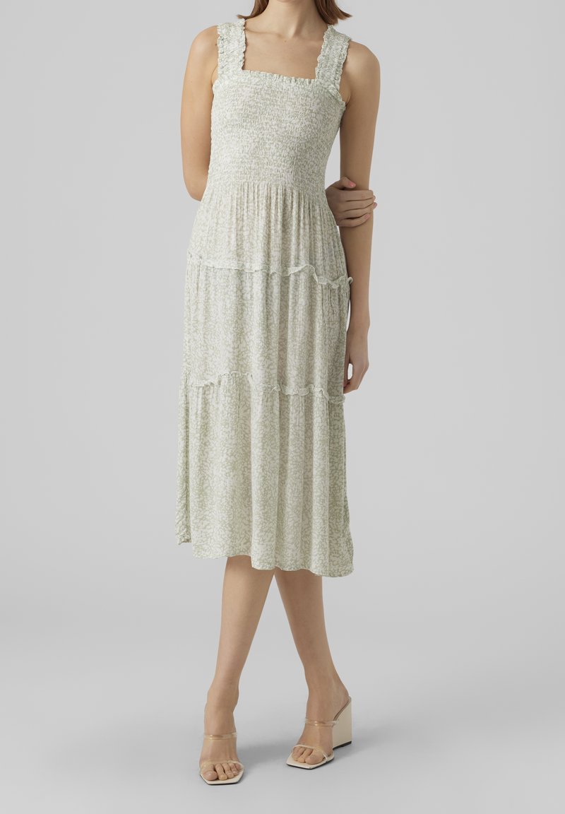 Vihreä kukkakuosiset mekko, jossa on neliönmallinen pääntie, rypytetty yläosa ja kerrokselliset röyhelöt; yhdistetty läpinäkyviin korkokenkiin.