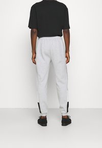 Šedé tepláky s volným střihem, elastickým pasem, černobílými bočními pruhy a žebrovanými manžetami. Doplněno černou obuví.