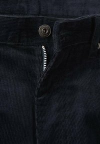 Los pantalones oscuros de pana cuentan con una cremallera oculta y cierre de botón metálico. La tela tiene una textura acanalada vertical que mejora la durabilidad.