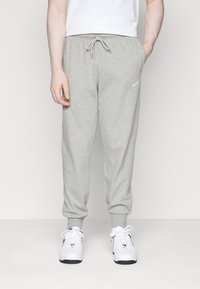 Gray sweatpants with a drawstring waist, cuffed ankles, and small white logo on the thigh. Smooth texture, casual design, unstructured fit.