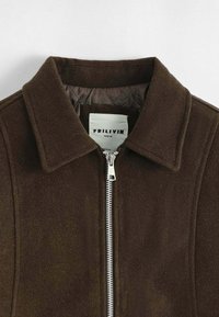 Veste en daim marron avec un col plat et une fermeture éclair argentée à l'avant. Intérieur doublé avec une texture lisse. Étiquette indiquant "FRILIVIN, PARIS."