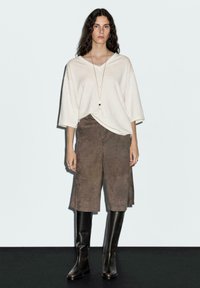 Cream v-neck oversized sweater with short sleeves, paired with brown suede culottes and knee-high black leather boots. Simple gold necklace accent.