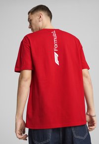 Rød bomulds t-shirt med et hvidt "Formula 1" logo trykt lodret på ryggen. Korte ærmer og en afslappet pasform.