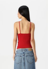 Top sin mangas rojo de canalé con tirantes finos, combinado con una falda de mezclilla de talle alto. El top tiene un diseño ajustado, mostrando una textura suave.