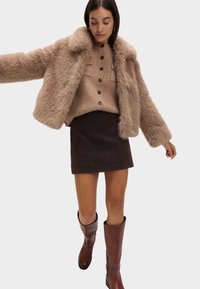 Faux fur beige jakke, strikket tan sweater med knapper, ternet brun nederdel og brune knæhøje støvler. Velegnet til køligt vejr.