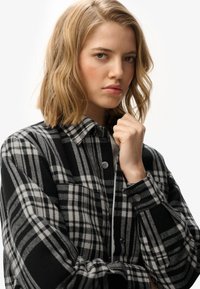Black and white plaid flannel jacket with a collar, button closures, and long sleeves. Fabric appears soft with a textured finish.