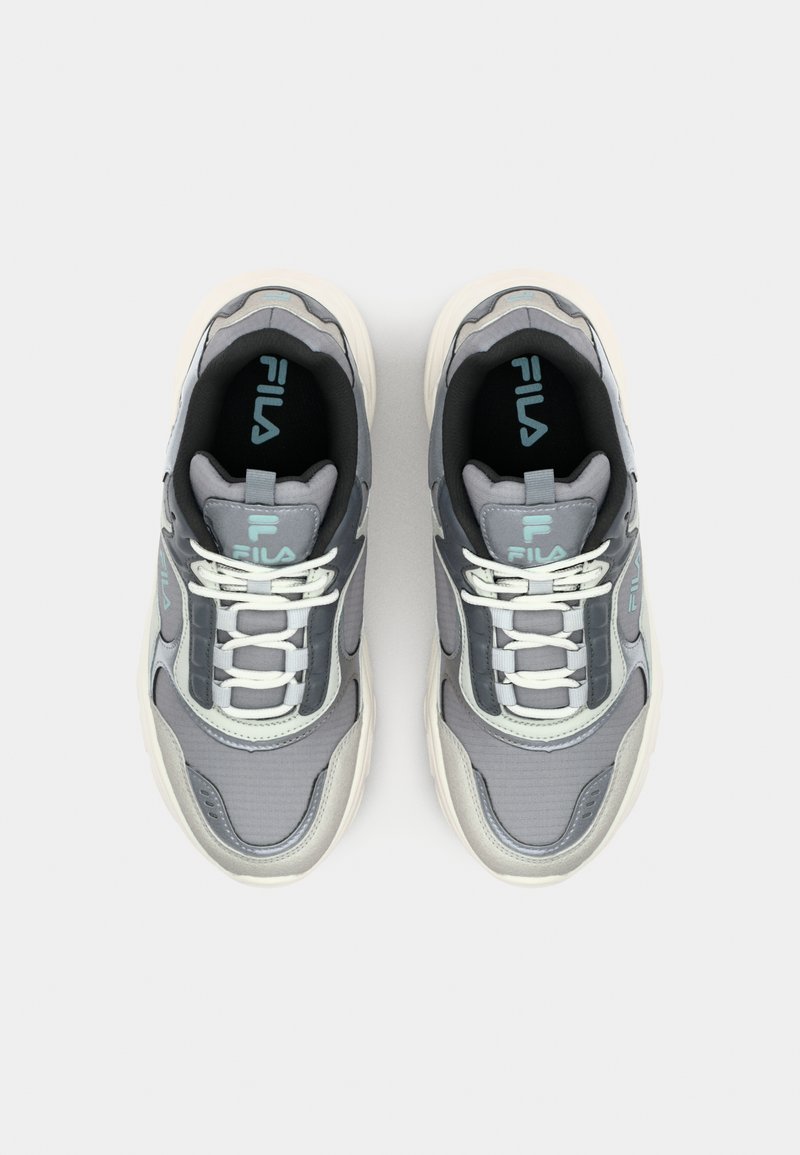 Baskets de sport grises avec une tige texturée, lacets blancs, accents turquoise et un design de semelle épaisse. Logo affiché sur la languette.