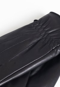 Guante de cuero negro con una textura suave, que presenta costuras sutiles y detalles fruncidos en la parte posterior para un ajuste ceñido.