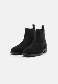 Schwarze Wildleder Chelsea-Stiefel mit elastischen Seitenpaneelen, runder Zehenpartie und Zugschlaufen. Flache Gummisohle. Einfaches und elegantes Design.