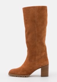 Bota alta de ante marrón con punta redondeada, superficie texturizada y un tacón de madera grueso. Presenta un diseño de costura superior suave.