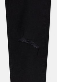 Pantalon en denim noir avec une zone usée aux bords effilochés, mettant en valeur la texture du tissu et le design décontracté.
