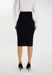 Schwarzer Bleistiftrock mit einer taillierten Silhouette und glatter Textur, kombiniert mit einer weißen Bluse und schwarzen High Heels.