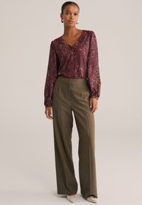 Blouse bordeaux à motif floral et manches bouffantes, assortie à un pantalon large taille haute en olive vert, complété par des chaussures crèmes à bouts carrés.