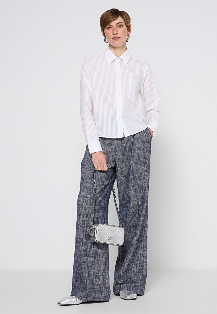 Biała, paskowana koszula z guzikami i kieszonką na piersi, zestawiona z szerokimi, ciemnoniebieskimi spodniami dżinsowymi. Dodatki to srebrna torebka i buty.