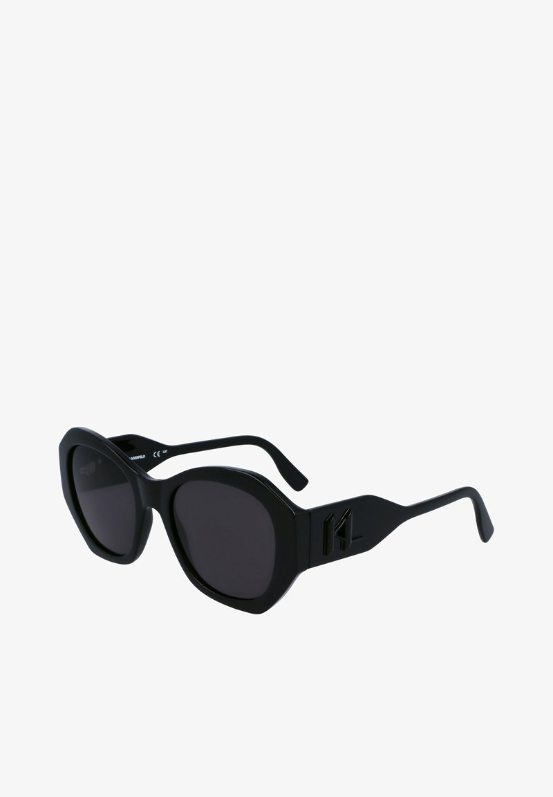 Melnas saulesbrilles ar oktagona formu, tonētiem stikliem, teksturētām kājām un zīmola logotipa detaļu sānos. Matēta apdare.