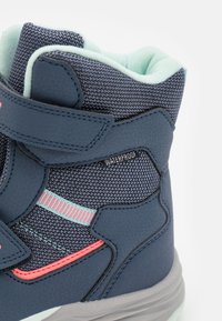 Donkerblauwe waterdichte laars met textuurstof, contrasterende roze en muntgroene accenten, verstelbare riem en een gevoerde binnenkant.