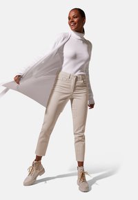 Witte geribbelde coltrui, beige corduroy broek met voorzakken, en crèmekleurige combat boots met veters en textuurzolen.