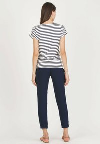 Gestreepte navy en witte T-shirt met korte mouwen, gecombineerd met slim-fit navy broek. Het model draagt platte sandalen en toont een deel van de enkel.