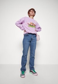Sudadera morada con un gráfico de cachorros, combinada con vaqueros azules. El calzado es de color rosa y negro con cordones verdes. Sombrero de cubo con estampado floral.